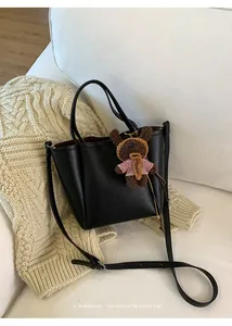 Détail du sac seau en cuir grainé noir avec un charm d'ours brun sur un canapé douillet
