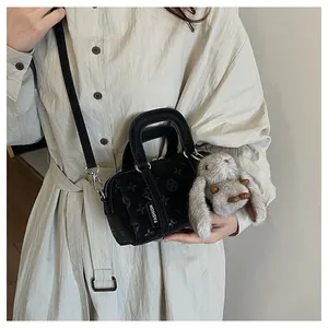 Detail of black embossed cylindrical baguette bag with plush bunny charm and strap