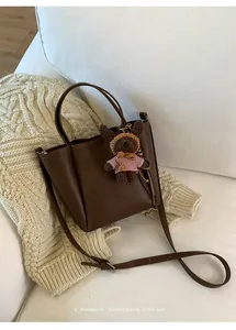 Détail du sac seau en cuir marron foncé avec breloque ours et finition texturée