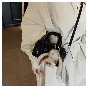 Close-up of black embossed baguette bag with cute plush bunny charm and crossbody strap