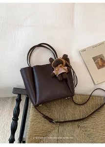 Détail d'un sac cabas en cuir marron foncé avec un ours peluche dans un décor rétro