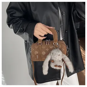 Close-up of brown embossed cylinder bag with a gray plush rabbit charm and silver zipper