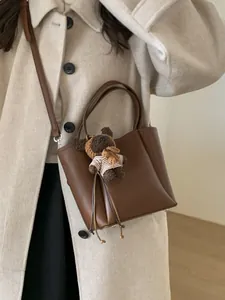 Sac seau marron en cuir avec pendentif ours et clous argentés porté par un mannequin élégant