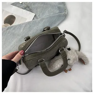 Close-up of olive green suede cylinder bag with floral embossing and plush bunny charm