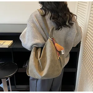 Detailansicht der khakifarbenen Wildledertasche mit weicher Textur und Plüschanhänger am Gurt
