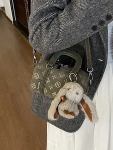 Dark green baguette bag with vintage patterns and a rabbit charm on a grey blazer model