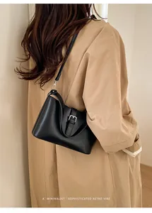 Vue latérale d'un sac hobo noir minimaliste porté avec un trench-coat classique