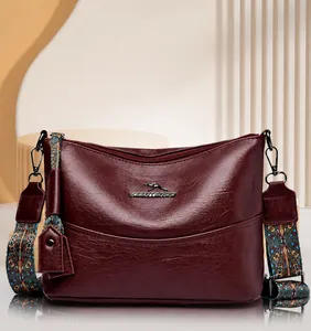 Detail van bordeauxrode handtas met vintage geborduurde brede schouderriem van leer