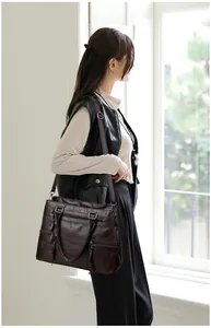 Detail of dark brown soft leather shoulder bag with multiple zip pockets shown on model