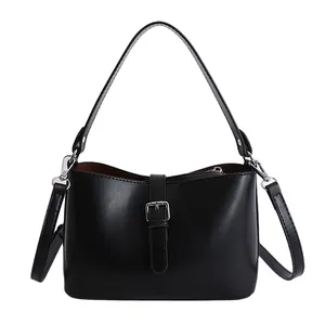 Sac à bandoulière minimaliste noir pour femme avec poignée et sangle amovible sur fond blanc