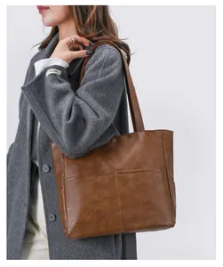Brown soft leather tote bag with functional pockets worn over a grey wool coat