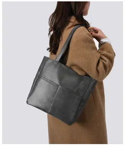 Detail of grey leather tote bag showing soft lychee texture and stitching on brown coat