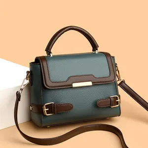 Green and brown leather handbag with gold metal buckle on a white geometric stand