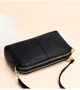 Detail of black pebbled leather crossbody bag with dual golden zippers and slim strap