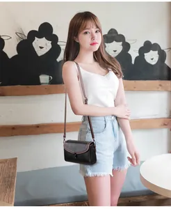 Detailed view of the black leather texture and brown adjustable strap on a small square bag