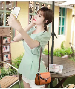 Detail of tan pebble leather crossbody bag with silver buckle worn by a model outdoors