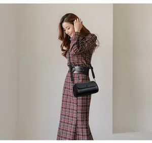 Détail d'un sac cylindrique en cuir souple noir porté sur une robe à carreaux chic