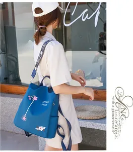 Blue oxford backpack detail featuring pink floral embroidery and colorful woven shoulder strap