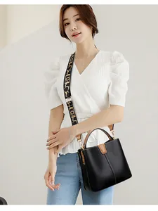 Detail of black pebbled leather bucket bag with brown handle and patterned wide strap