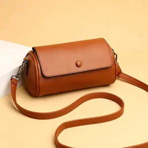 Sac cylindre élégant en cuir caramel avec rabat sur fond chaud et accessoires rétro