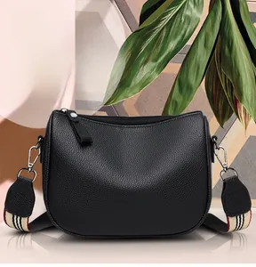 Close-up of black litchi grain leather saddle bag with striped wide shoulder strap