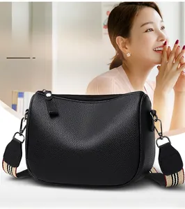 Detail of black pebbled leather saddle bag with striped fabric wide shoulder strap