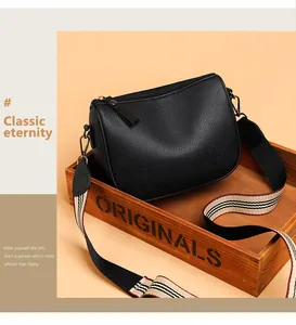 Detail view of black pebble leather saddle bag with striped wide fabric shoulder strap
