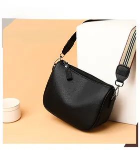 Close-up of black pebble leather saddle bag featuring a red and beige striped wide strap