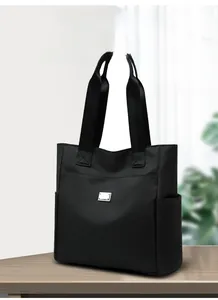 Macro shot of durable black nylon tote bag featuring a silver metal logo and side pockets
