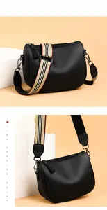 Close-up of black lychee leather saddle bag with striped woven strap and metal hardware