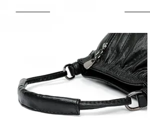 Detail of ergonomic curved handle on black lychee leather bag with metal hardware