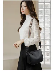 Close-up of a black lychee texture saddle bag featuring a striped wide fabric shoulder strap