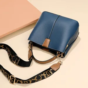Navy blue bucket bag with brown handles and a wide jacquard strap on a beige background