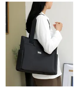 Close-up of a black high-capacity nylon tote bag featuring a minimalist metal logo plate