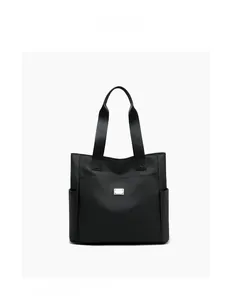Detailed close-up of large black nylon tote bag with silver metal plate and side pockets