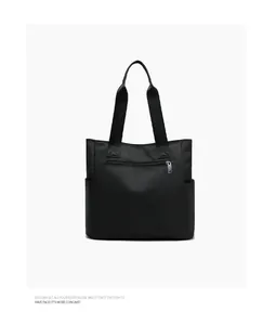 Close-up of black nylon tote bag featuring front silver zipper pocket and sturdy straps