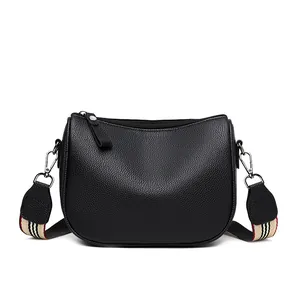 Black pebbled PU leather saddle bag with a striped woven wide shoulder strap on white base