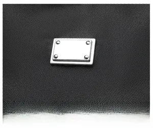 Detail of silver rectangular metal plaque with rivets on black textured nylon handbag