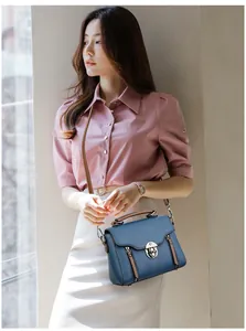 Detail view of a navy blue pebble leather crossbody bag with a metal turn-lock and brown trim
