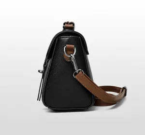 Zijaanzicht van tweekleurige crossbodytas met zwarte lychee textuur en bruin lederen riem