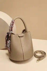 Detail of khaki pebbled leather bucket bag with silk scarf handle and gold hardware