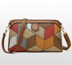 Close-up of gray-brown geometric patchwork leather crossbody bag with golden clover hardware