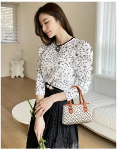 Detail einer eleganten kleinen Handtasche mit geometrischem Blumenmuster und braunen Tragegriffen