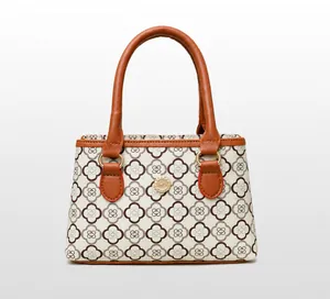 Nahaufnahme der cremeweißen Handtasche mit braunem Kleemuster und metallischem Rundlogo