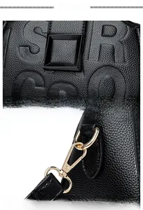Close-up of black litchi leather bag with embossed letters and golden metal hardware