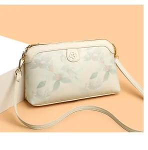 Dettaglio ricamo floreale e logo a quadrifoglio dorato su borsa a tracolla beige chic
