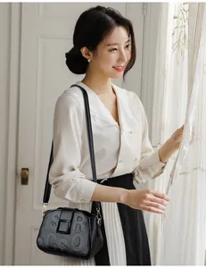 Detail of black lychee grain leather crossbody bag with stylish letter embossing on flap