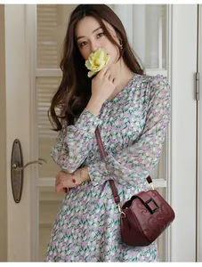 Detail of burgundy leather crossbody bag with embossed letters and floral dress styling