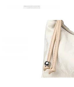 Detailed view of cream dumpling bag featuring long leather puller and silver bead accent