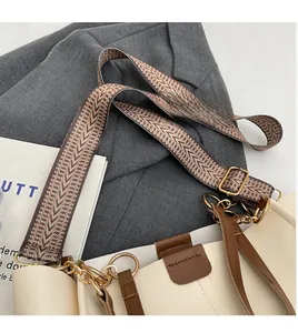 Detail of the woven wide shoulder strap with golden metal buckle on a beige handbag